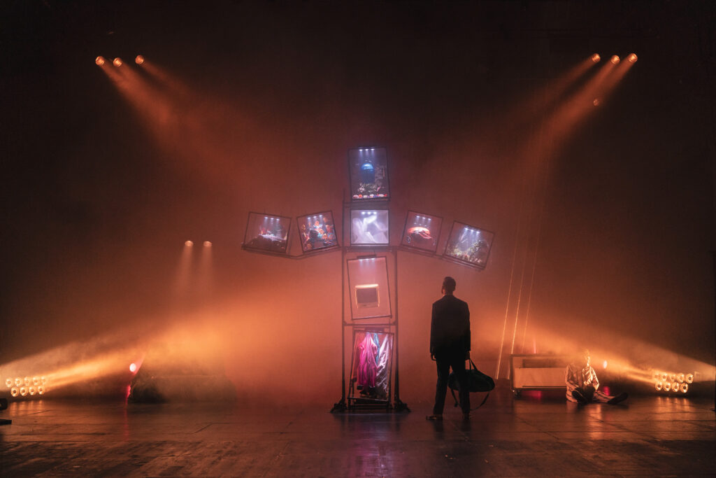 une croix faite en écran en fond, un comédien devant elle avec une création de costume à Bordeaux